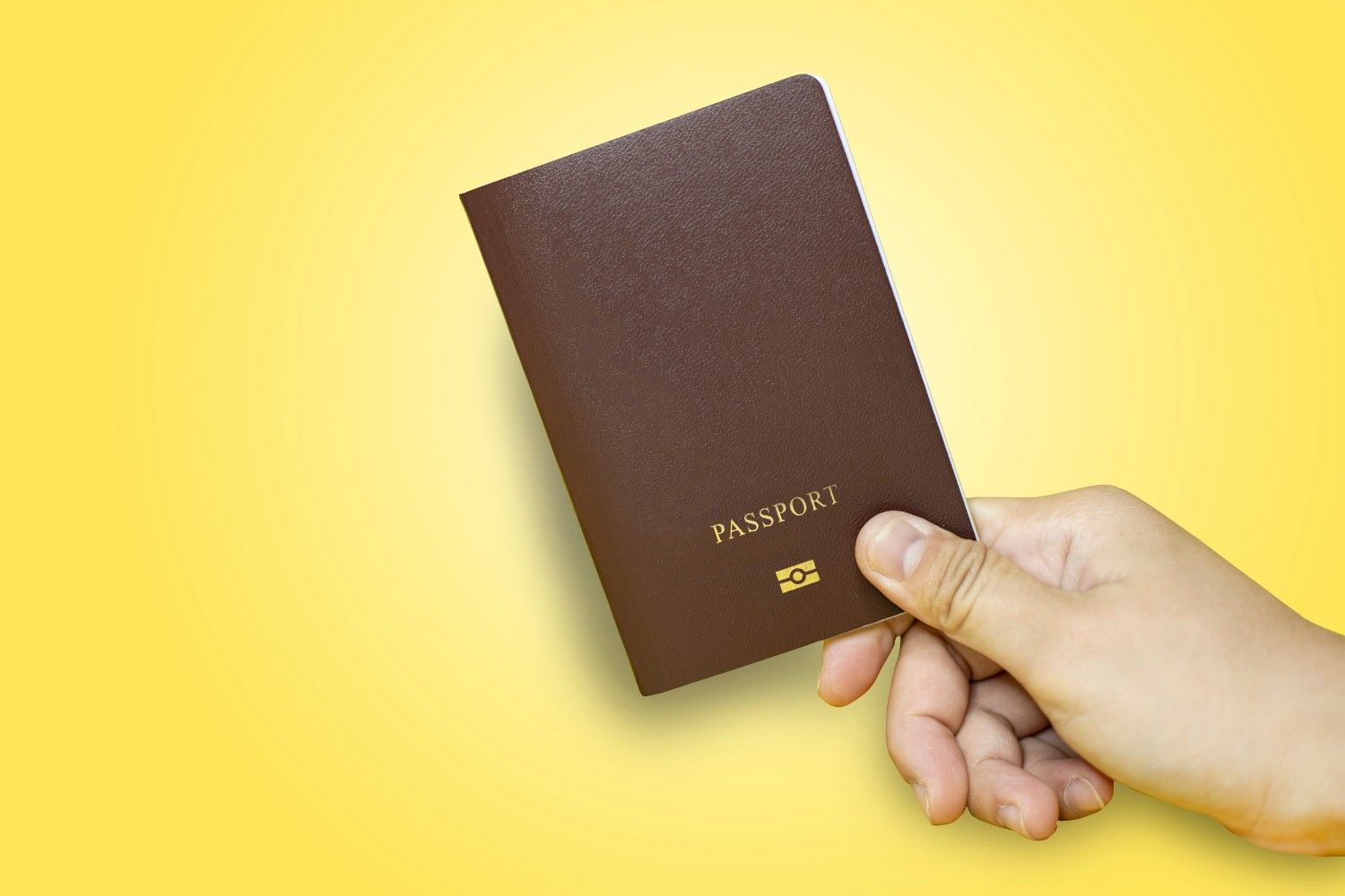 Hand Holding Passport In Brown With Yellow Background