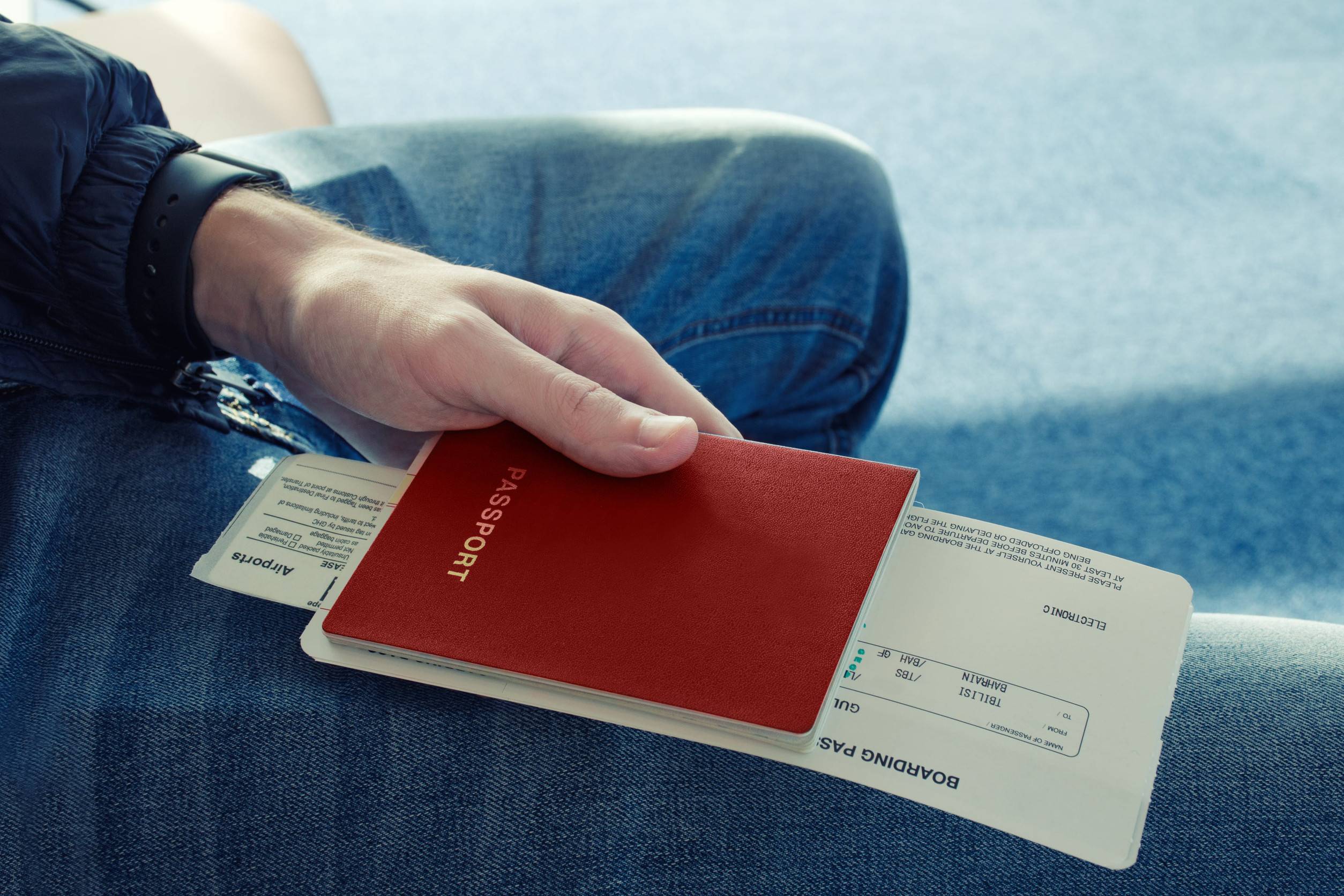 Man In Blue Jeans Sits And Holds In His Hand Passport